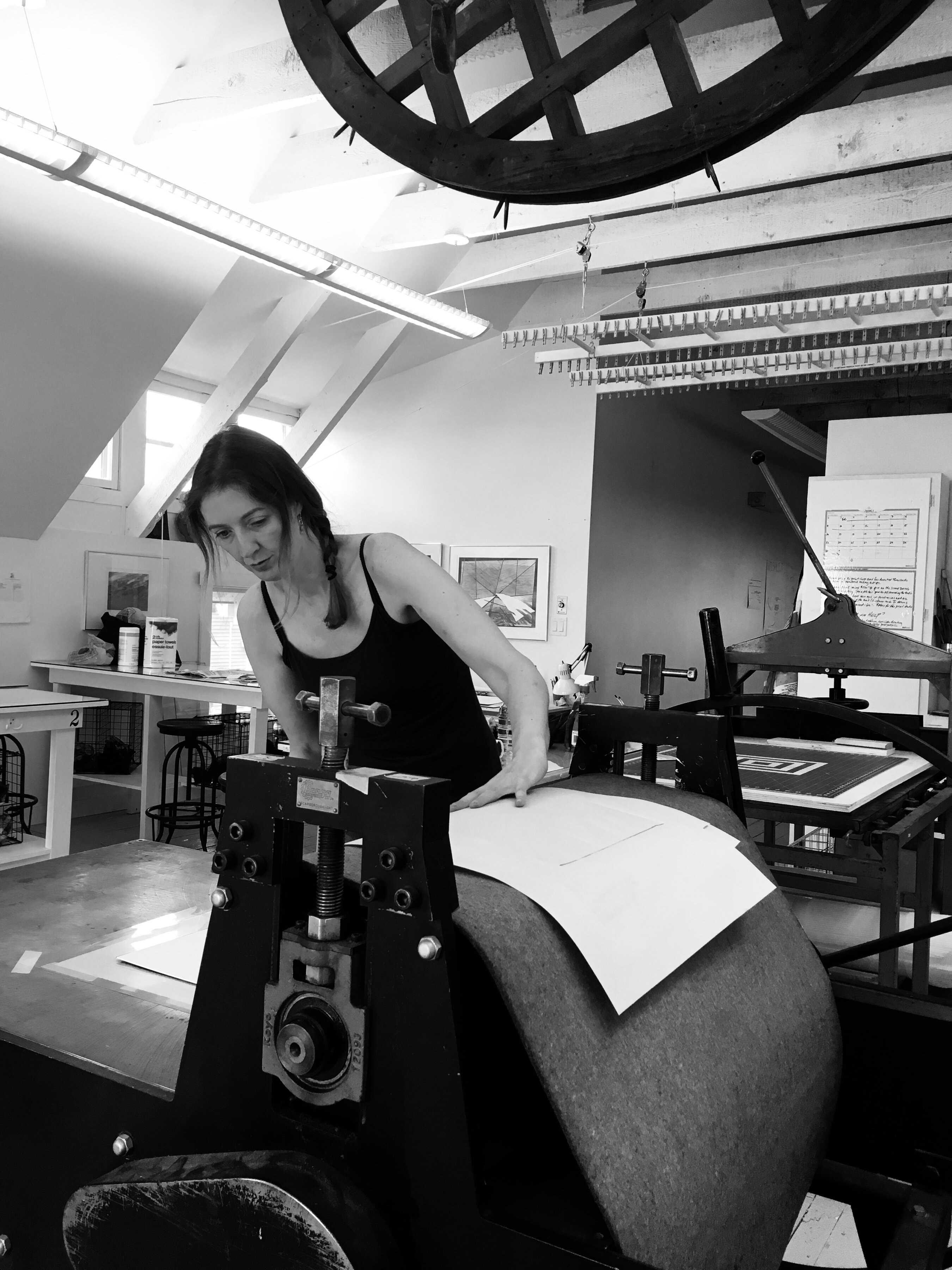 Black and white photo of artist Fae Kilburn working in her studio using an etching press