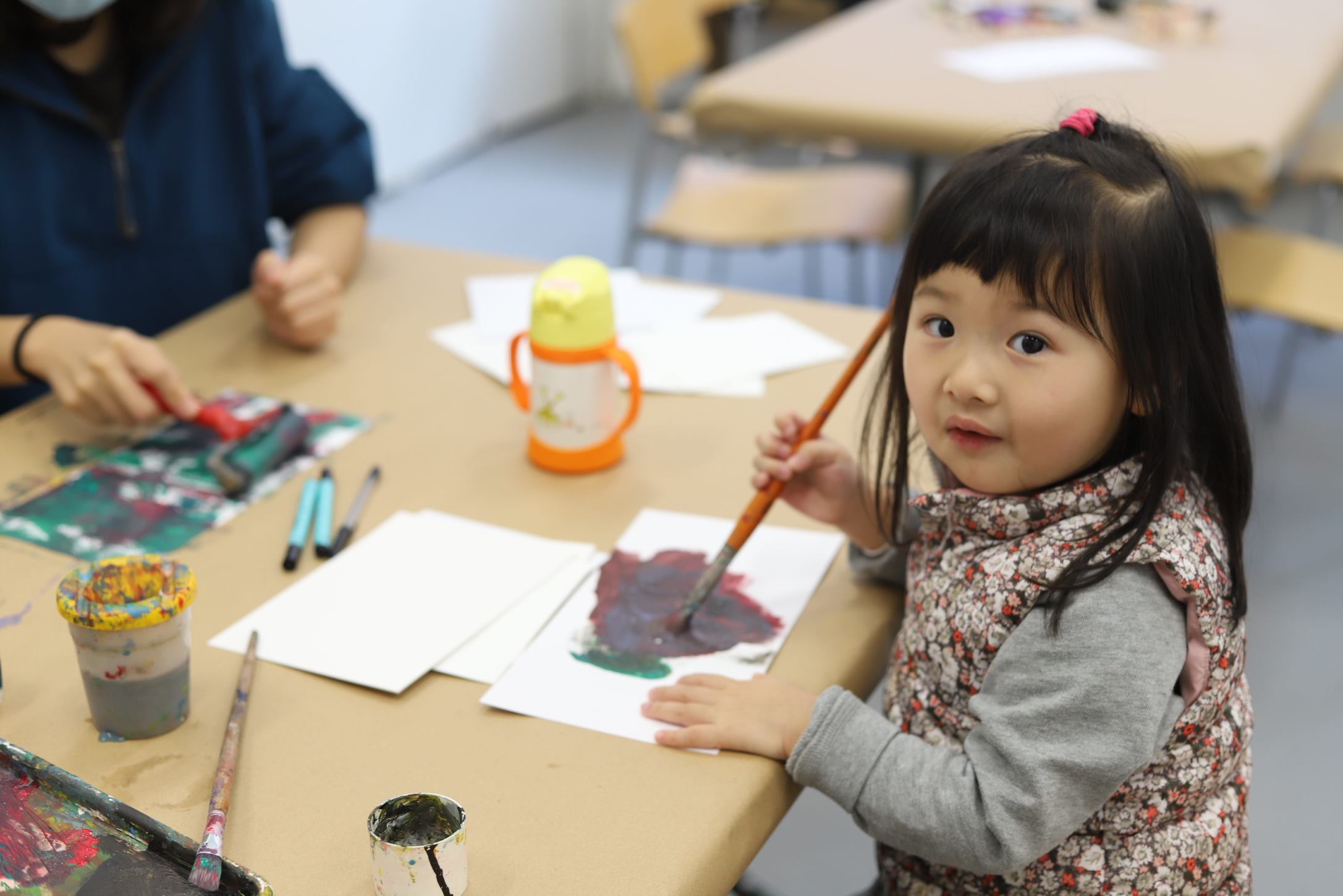 Photo of a young child painting while looking at the camera.